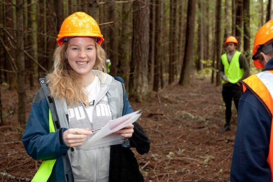 Student facing camera holding notepaper in pine forest