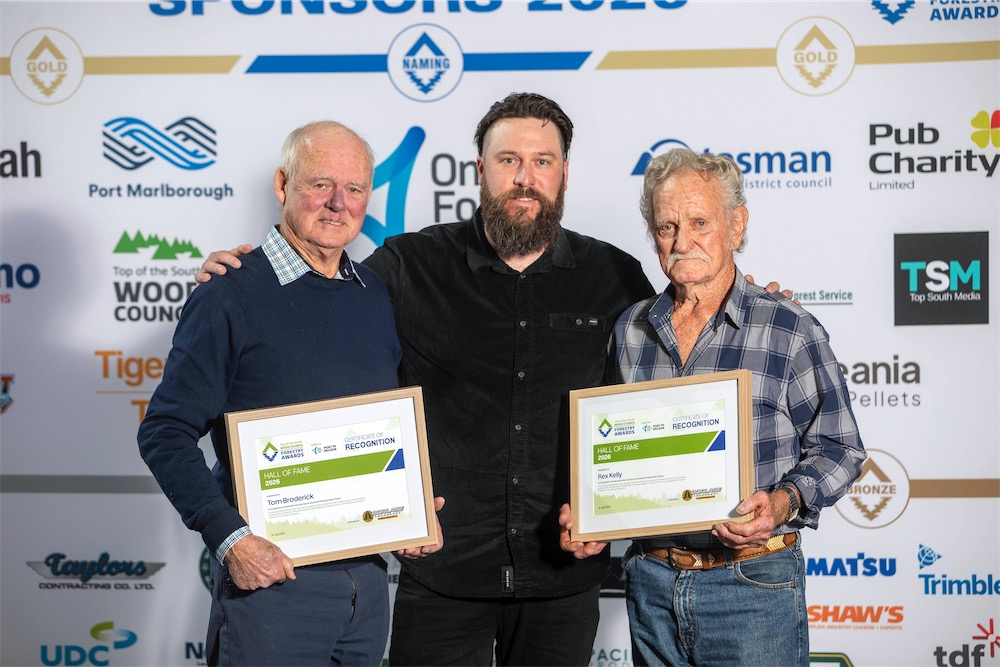 Three men stand in front or a sponsor board. Two of the men hold a framed certificate for their induction into the Hall of Fame by Steve Borlase, Business Manager from Borlase Transport